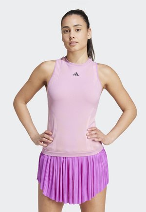 Débardeur de sport rose à design sans manches avec logo, associé à une jupe plissée rose. Texture lisse, silhouette ajustée.
