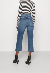 Högmidjade blå denimjeans med en kort, bred benklippning. Femfickorsdesign och rå kantdetalj. I kombination med svarta ankelskor.