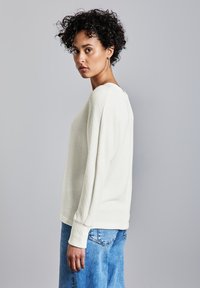 Maglione beige chiaro con texture, maniche lunghe, scollatura arrotondata e vestibilità rilassata, abbinato a jeans in denim blu.
