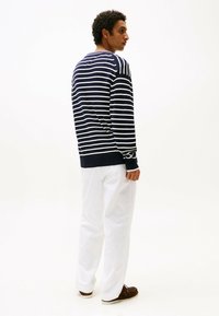 Maglione a righe blu navy e bianche con maniche lunghe, polsini e orlo a coste. Indossato con pantaloni bianchi e mocassini marroni.