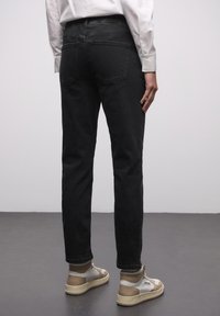 Černé džíny z denimu s rovnými nohavicemi. Mají zadní kapsy, středně vysoký pas a ohrnuté lemy. Kombinovány s béžovými a bílými teniskami.