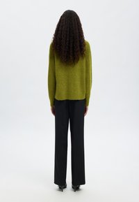 Suéter verde de punto con un ajuste holgado, combinado con pantalones de pierna ancha negros y zapatos de tacón. Tejido texturizado y silueta relajada.
