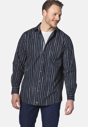 Marineblaue Button-Up-Bluse mit weißen vertikalen Streifen, langen Ärmeln, Kragen, einer Brusttasche und einem strukturierten Stoff. Kombiniert mit dunkelblauen Jeans.