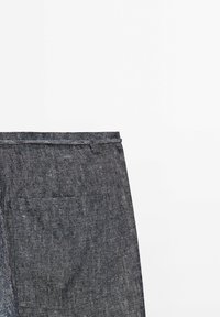 Dark denim pants with a textured surface, featuring a single back pocket and belt loops, displayed against a white background.
