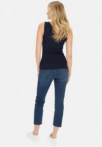 Granatowy top bez rękawów z marszczeniami, w połączeniu z jeansami o średnim stanie i białymi sneakersami. Tkanina wydaje się gładka i elastyczna.