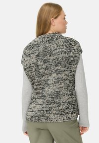 Pull sans manches tricoté dans des tons noir et beige, avec un motif texturé. Coupe décontractée avec un col rond et des côtés ouverts.