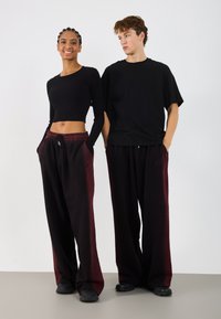 Crna rebrasta crop majica u kombinaciji s bordo hlačama na vezanje, koji imaju opušteni kroj i bočne džepove, uparen s crnim cipelama.