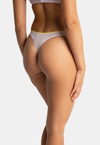 String lilas fin avec une ceinture élastique jaune, présentant une finition transparente et une couverture minimale. Texture lisse et coupe haute sur les jambes.