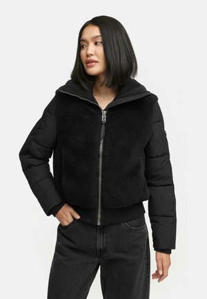 Zwarte cropped jacket met een pluche, textuurfront en gladde mouwen. Voorzien van een capuchon en zilveren rits, gecombineerd met een donkere spijkerbroek.