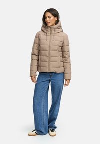 Pufferjack in lichtbeige met een capuchon, voorzien van een gestikt ontwerp en een rechte snit. Gecombineerd met brede blauwe jeans en sneakers.
