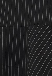 Černá tkanina s alternativními úzkými a širokými bílými pruhy. Hladká textura s viditelným šitím, uspořádaná v geometrickém vzoru.