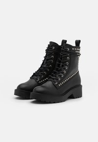 Czarne skórzane buty wojskowe z wiązanym zapięciem, zdobieniami w formie ćwieków, masywnym obcasem, teksturowaną powierzchnią oraz solidną gumową podeszwą.