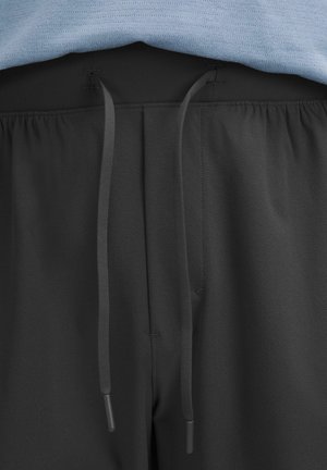 Schwarze Sporthosen mit elastischem Bund, Kordelzug und glatter Textur. Ein hellblaues Shirt ist teilweise sichtbar oben.