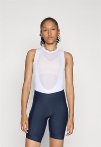 Hvid ærmeløs cykelbluse med mesh-detaljer og marineblå cykelshorts, der har en tætsiddende pasform og tekstureret stof.