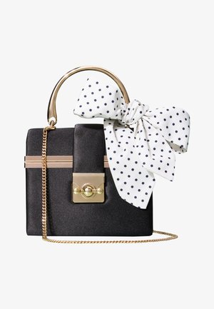 Sac à main rectangulaire noir avec poignée et chaîne dorées, avec un foulard blanc à pois noirs noué en nœud sur la poignée.