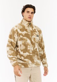 Fleece halv-zip pullover i beige og creme, med en tekstureret, fluffy overflade og en brystlomme med et logo mærke.