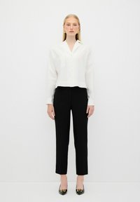 White, long-sleeve blouse with a collar, paired with black, tailored pants. Black shoes feature a gold accent. Clean and minimalist design.