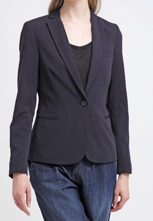 Blazer bleu marine avec un bouton, revers crantés et poches latérales ; associé à un haut noir et un jean bleu pour le contraste.