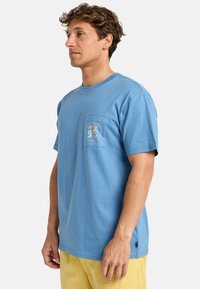 Light blue cotton t-shirt with short sleeves, round neck, and a pocket. Features a colorful palm tree graphic on the pocket.