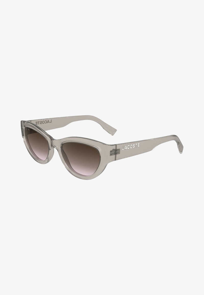 Óculos de sol cinzentos em formato de gato com lentes degradê, apresentando uma armação transparente e o logótipo "LACOSTE" na haste.