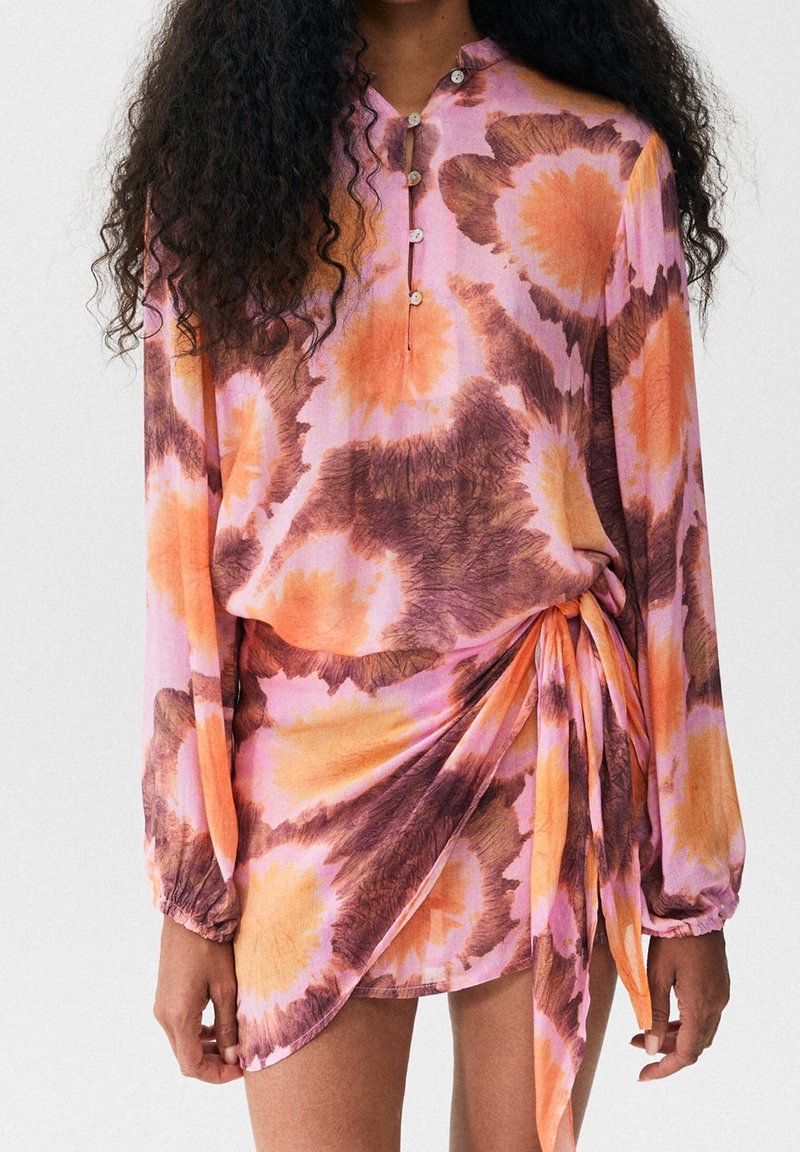 Long-sleeve, tie-front dress in pink, orange, and brown tie-dye fabric with a relaxed fit and buttoned neckline detail.
