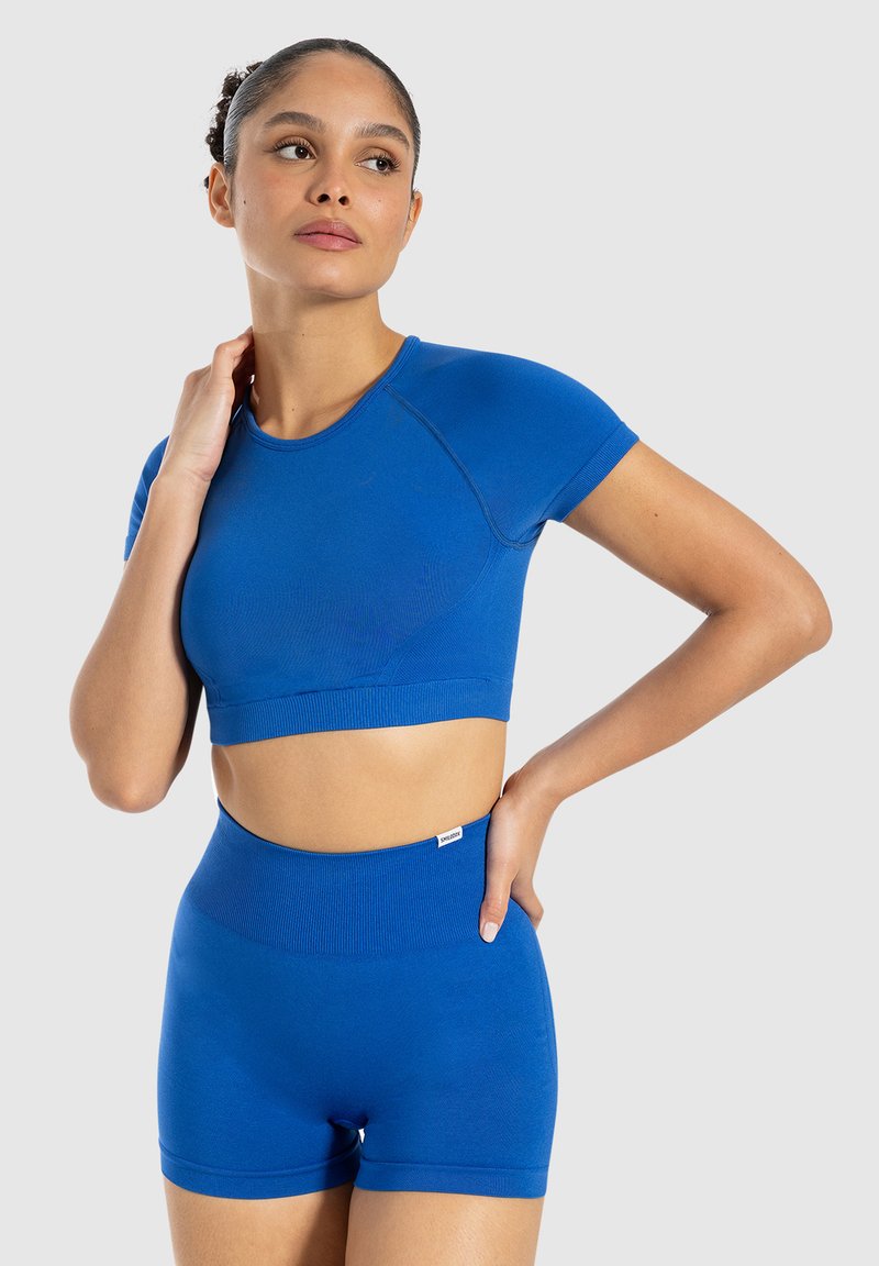 Cropped top sportivo blu con maniche corte, abbinato a pantaloncini a vita alta. Tessuto liscio ed elastico con una texture a coste e design aderente.