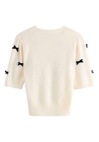 Maglione lavorato a maglia color crema con maniche a sbuffo corte, caratterizzato da fiocchi neri sulle maniche. La trama appare morbida con un orlo a coste.
