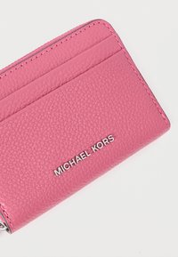 Ροζ δερμάτινη θήκη καρτών με υφή στην επιφάνεια, πολλαπλές θήκες για κάρτες και μεταλλικό λογότυπο "MICHAEL KORS" στο μπροστινό μέρος.