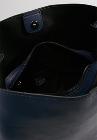 Sac à main en cuir bleu foncé avec intérieur noir, doté d'une poche zippée et d'une fermeture magnétique argentée.