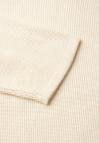 Tessuto testurizzato bianco sporco con motivo a costine; include un bordo della manica piegato che mostra una finitura a maglia liscia e un sottile dettagli di cucitura.