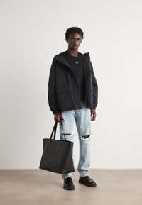 Black hooded jacket with a zip, black sweater, distressed light blue jeans, and a black tote bag with embossed "HUGO" logo; black shoes.