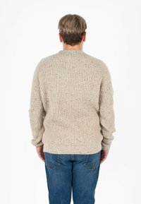 Beżowy sweter z ribbowanym splotem, okrągłym dekoltem, fakturowanym materiałem oraz opadającymi szwami na ramionach, w połączeniu z niebieskimi dżinsami.