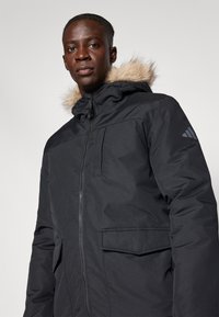 Μαύρο χειμερινό μπουφάν με κουκούλα με γούνα, που διαθέτει μπροστινό φερμουάρ και δύο πλαϊνές τσέπες. Απαλή υφή και πρακτικός σχεδιασμός.