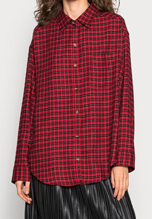 Chemise à carreaux rouge et noir avec un boutonnage à l'avant, des manches longues et une poche poitrine. Fabriquée dans un tissu avec une finition douce et légèrement texturée.