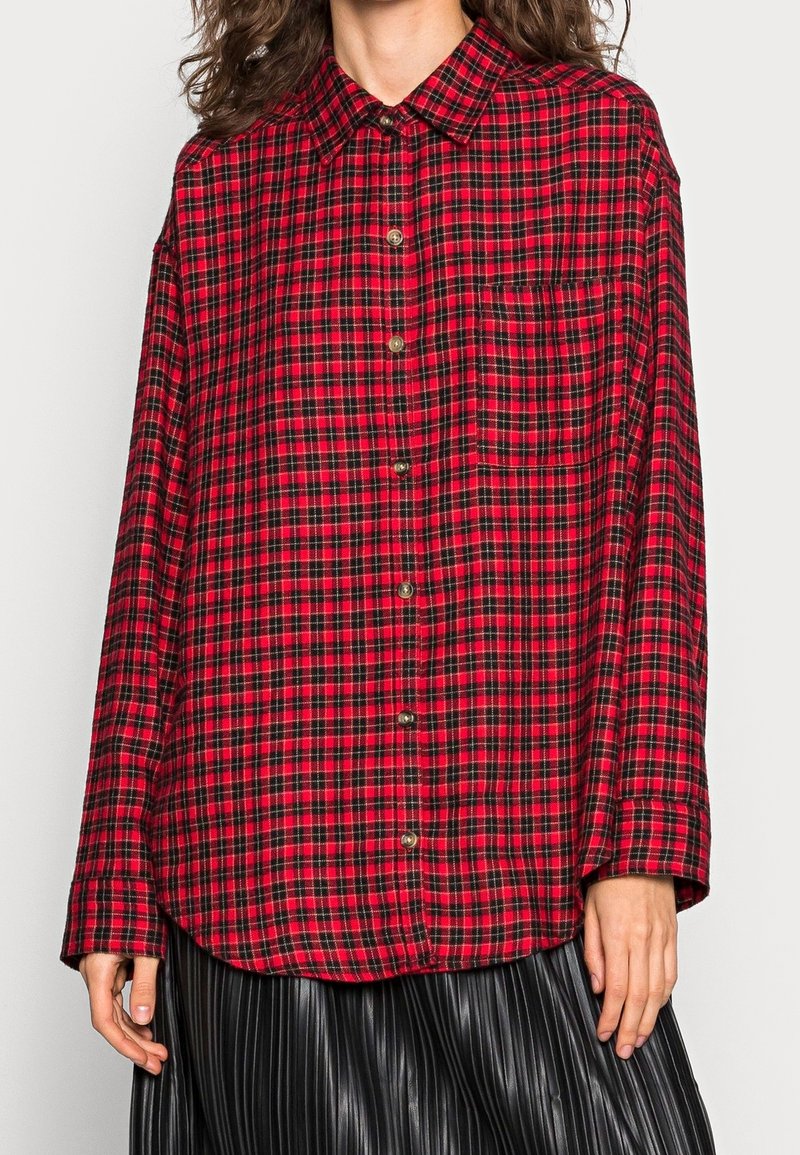 Camicia a quadri rossa e nera con abbottonatura frontale, maniche lunghe e taschino sul petto. Realizzata in tessuto con una finitura morbida e leggermente testurizzata.