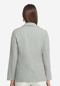 Gråtexturerad blazer med krage, långa ärmar och subtilt vävt mönster. Har en ryggslits för ökad rörelsefrihet.