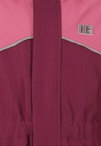 Bordeaux jacket met roze accenten, met een gladde textuur, elastische tailleband en reflecterende grijze rand. Label zegt "Maak je klaar om te spelen."
