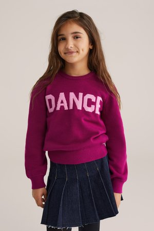 Fuksjowy sweter z napisem "DANCE" w jasnoróżowych literach, prążkowany dekolt i mankiety; w połączeniu z ciemnoniebieską plisowaną spódnicą.