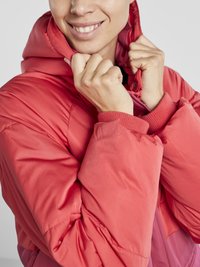 Casaco vermelho acolchoado com capuz. Apresenta fecho de correr na frente, punhos canelados e textura de tecido suave. Detalhes de costura visíveis nos ombros.
