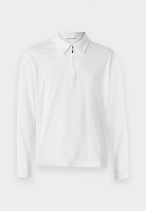 Bílá dlouhá polo košile s límečkem a polo zapínáním vpředu. Hladká textura a jednoduchý design bez dalších vzorů.