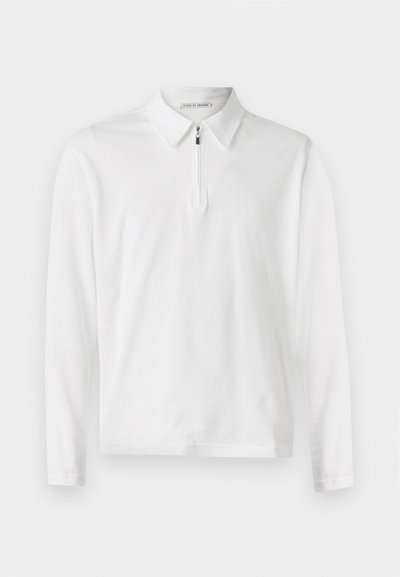 Λευκό πουκάμισο polo με μακριά μανίκια, γιακά και με μισό φερμουάρ στο μπροστινό μέρος. Λείος υφασμάτινος ιστός και απλός σχεδιασμός χωρίς επιπλέον σχέδια.