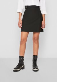 Musta, vartalonmyötäinen minihame, jossa on sivuhalkio, valmistettu sileästä materiaalista. Yhdistetty mustiin, paksulla pohjalla varustettuihin nauhakenkiin.