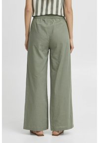 Pantaloni larghi di colore verde chiaro realizzati in un tessuto morbido con una vita elastica. Nessun motivo o dettaglio hardware visibile. Orlo piatto.