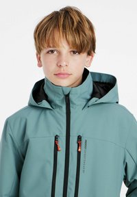 Helle türkisfarbene wasserdichte Jacke mit hohem Kragen, schwarzen Akzenten und zwei mit Reißverschluss versehenen Vorderaschen. Verfügt über eine abnehmbare Kapuze und kontrastierende Reißverschlüsse.