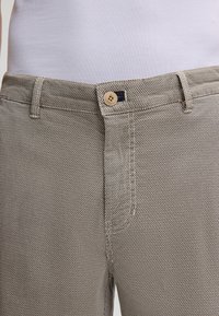 Pantaloni beige a fantasia in tessuto testurizzato, dotati di chiusura con bottone e un piccolo accento blu navy in vita.