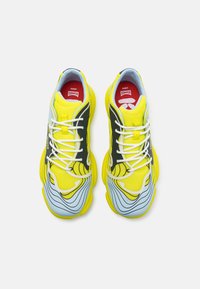 Yellow and black athletic shoes with a mesh upper, wavy blue accents, white laces, and red branding. Thick rubber sole with traction pattern.