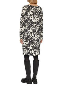 Robe à manches longues blanche avec un motif floral noir. Dotée d'un col rond et d'une légère ouverture à l'arrière. Portée avec des bottes noires jusqu'aux genoux.