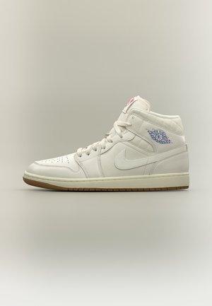 Fehér magas szárú Nike Air Jordan sportcipő kék logóval a bokánál és gumitalppal, világosszürke háttéren.