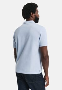 Jasnoniebieska koszulka polo z kołnierzykiem i krótkimi rękawami, z prostym dołem i bocznymi rozcięciami, wykonana z miękkiego, teksturowanego materiału.
