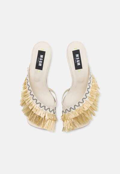 Beige open-toe heels with a fringe detail in light gold and black stitching. The insole features a logo label in black and white.